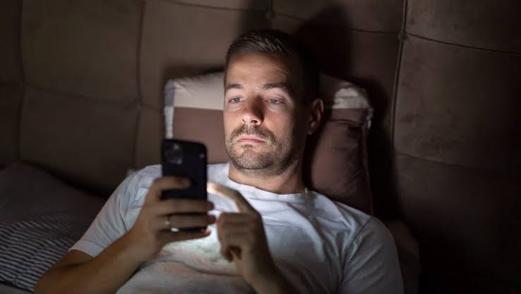 An adult scrolling on a phone in bed late at night